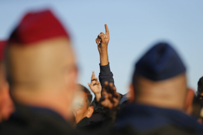 Migrants gesture in front of police as they wait for buses at collection point in Roszke