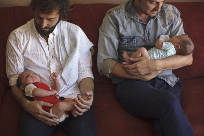 Luis Delgado holds son Marco as husband Antonio Ferndandez holds their daughter Olivia, at their home in Cancun