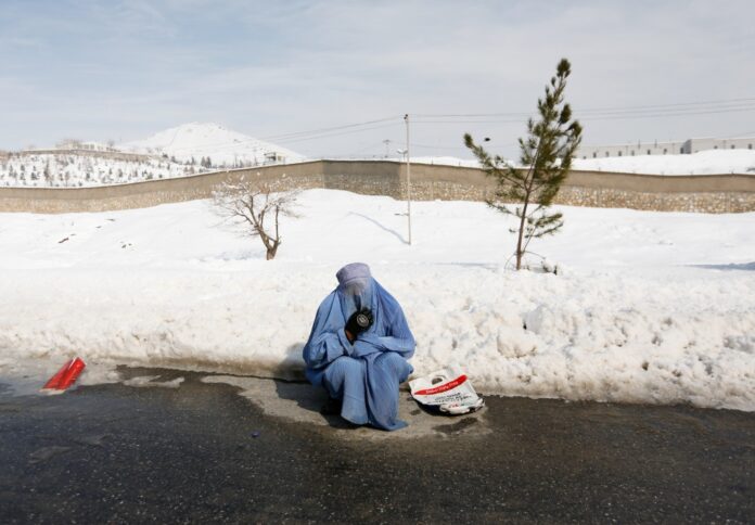 An Afghan woman clad in burqa begs in snow-covered street on the outskirts of Kabul