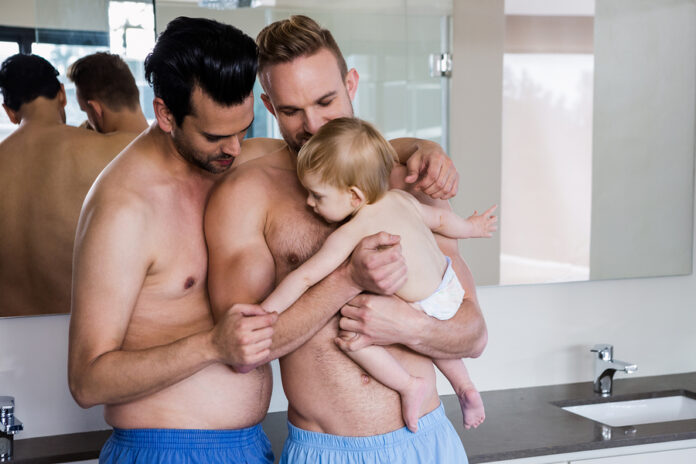 Happy gay couple holding their child in bathroom
