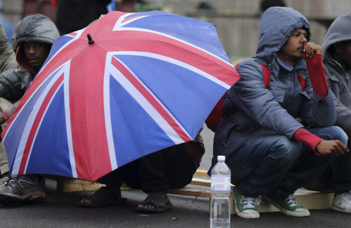 An Eritrean migrant takes cover from the rain under an umbrella during the daily food distribution at the harbour in Calais