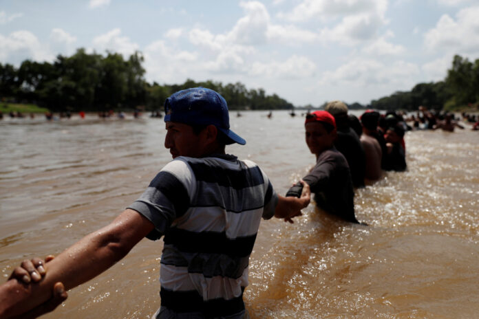 Migrants, part of a caravan traveling to the U.S., form a human chain to help fellow migrants cross the Suchiate river, a natural border between Guatemala and Mexico, in Ciudad Hidalgo